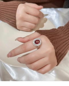 Detailed view of vintage silver ring with oval red gemstone and zircon halo on hand