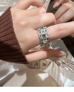 Detail of silver hollowed ring featuring three emerald green square gemstones on hand