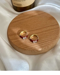 Detalle de pendientes de aro dorados con esmalte rojo y circón sobre seda