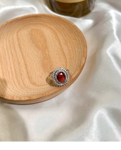 Macro shot of silver ring featuring oval red gemstone surrounded by brilliant zircon crystals
