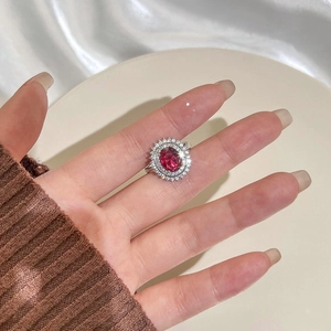 Vintage oval ruby red gemstone ring with crystal halo on woman's hand with soft fabric