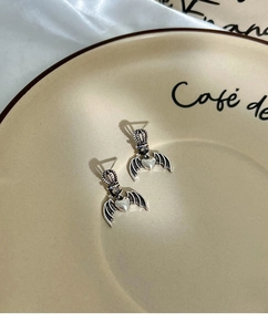 Macro detail of gothic crown and devil wing heart earrings on vintage ceramic display