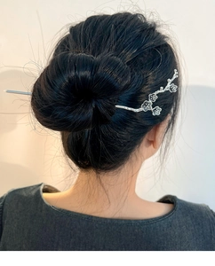 Detailed view of silver plum blossom hair pin styled in a sleek black hair bun for women