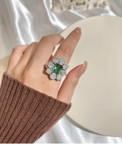 Gros plan d'une bague fleur émeraude avec pétales argentés et cristaux au doigt