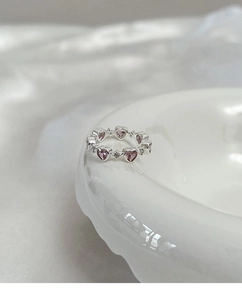 Macro detail of the silver ring band featuring pink heart-shaped stones and white crystals