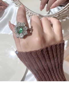 Détail d'une bague florale de luxe avec pierre vert émeraude et pétales de diamants