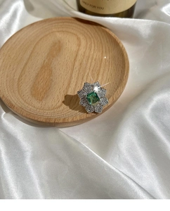 Vue de dessus d'une bague fleur émeraude sur un plateau en bois et soie blanche