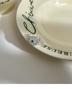 Close-up of a silver lace ring with green gemstone and pavé zircon stones on a ceramic plate