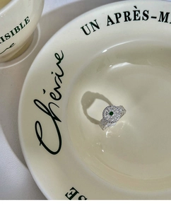 Macro shot of silver ring with green gemstone and heart-shaped shadow in ceramic dish