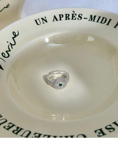 Close-up of silver lace ring with green gemstone on vintage ceramic tray