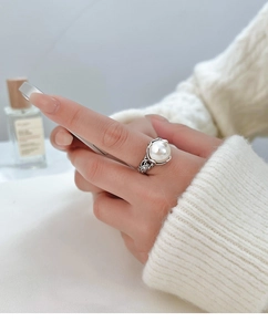 Detailansicht eines Vintage-Perlenrings am Zeigefinger mit barocken Hohlmustern aus Metall