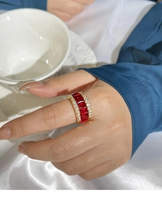 Détail d'une bague à pierres rouges et diamants blancs sur anneau doré portée par mannequin
