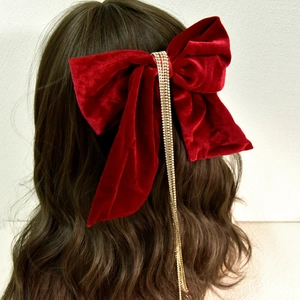Detail of red velvet bow hair clip with sparkling gold rhinestone tassels on wavy hair