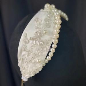 Detailed close-up of handmade bridal headband with pearls and sequins on white satin