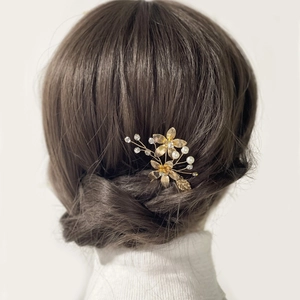 Elegant gold flower hair pin with white pearls and crystals worn on a bridal hairstyle