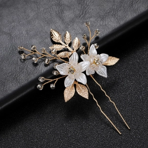 Macro detail of bridal gold hair pin with white flowers, crystal beads and metal leaves