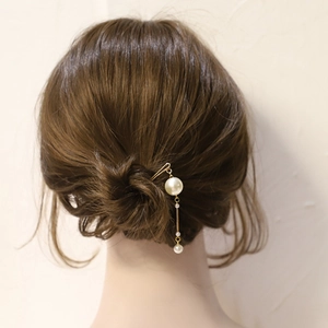 Détail d'une épingle à cheveux en U dorée avec pampille de perles portée sur un chignon