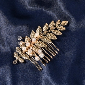 Makro-Detailansicht des goldenen Blatt-Haarkamms mit Perlen auf blauem Satinstoff