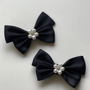 Détail de deux nœuds en satin noir avec fleur de perle et accents de strass centraux