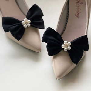 Détail d'un clip à chaussure en satin noir avec perles sur des talons aiguilles beiges
