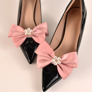 Détail d'escarpins en cuir verni noir avec nœuds en satin rose et ornements de fleurs en perles