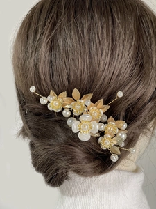 Detail of bridal hair pins set with white flowers, gold leaves and pearls on a model