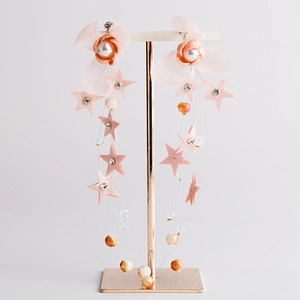 Orecchini a fiori rosa con stelle e perle su un supporto per gioielli in oro rosa