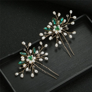 Detail of golden U-shaped hair pins with green crystals and white pearls on wood