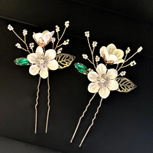 Détail d'épingles à cheveux de mariée avec fleurs blanches, gemmes vertes et feuilles