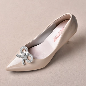 Close-up of sparkling rhinestone bow accessory on pointed-toe nude patent leather high heels