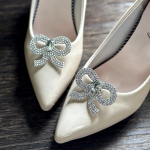 Macro detail of bridal shoe clips with sparkling rhinestone bow on off-white heels