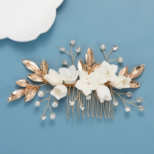 Elegant gold bridal hair comb with white ceramic flowers, pearls, and crystals on blue background