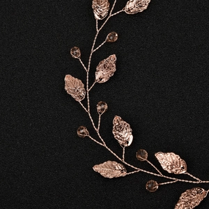 Detailed close-up of rose gold leaf and crystal bridal hair vine on black texture