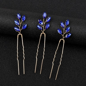 Vista macro di tre forcine a U dorate con cristalli blu a forma di foglia per sposa