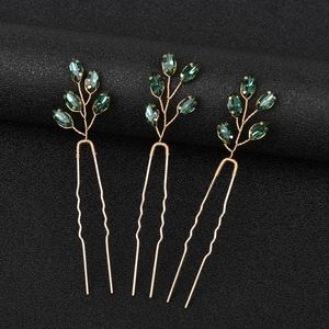 Dettaglio di tre forcine a U dorate con cristalli verde smeraldo dal taglio marquise