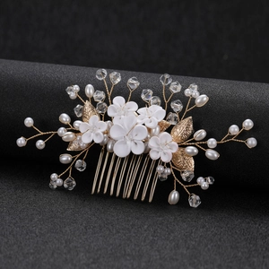 Close-up of white clay flowers and golden metallic leaves on a bridal hair comb