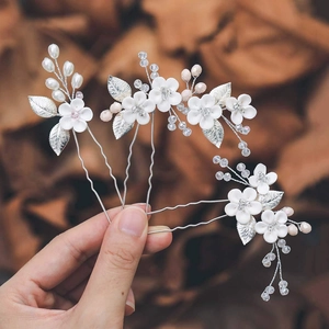 Detail of three-piece bridal U-shaped hair pins with white clay flowers and metal leaves