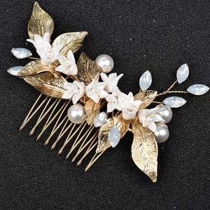 Macro view of gold alloy leaves, white ceramic flowers, and pearls on a bridal hair comb