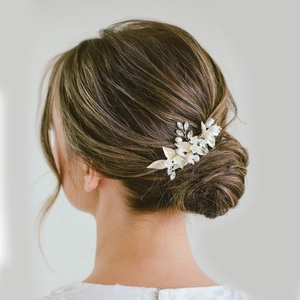 Bridal hair comb with white ceramic flowers and golden metal leaves on elegant updo hair