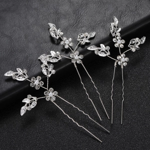 Close-up of three silver bridal hair pins with leaf patterns, rhinestones and pearls