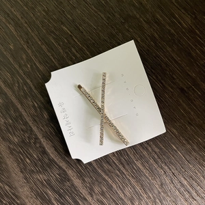 Barrette croisée élégante dorée avec strass scintillants sur carte de présentation