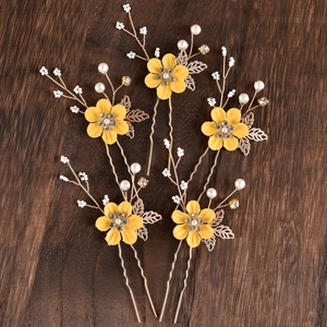 Close-up of five handmade bridal hair pins with yellow flowers, pearls and golden leaves