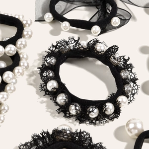 Gros plan sur chouchou en dentelle noire avec perles blanches élégantes sur fond beige