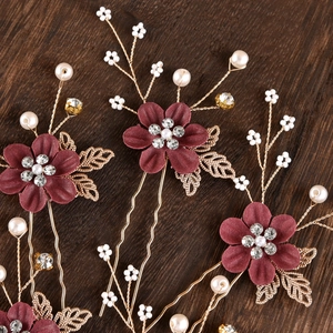 Close-up of handmade bridal hair pins with red fabric flowers and golden leaves