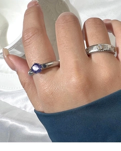 Detail of silver twisted ring with purple zircon and geometric band on silk fabric