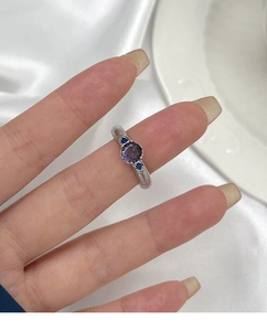 Macro view of a silver ring with a round purple gemstone and textured striped band