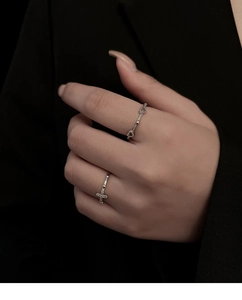 Detail of silver rings featuring a heart link band and a zircon-set cross on finger