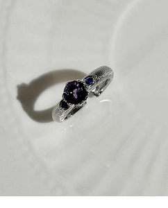 Detail of silver ring with round purple gemstone and blue teardrop side stones