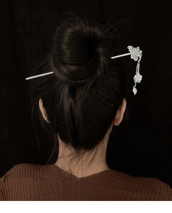 Gros plan d'un pic à cheveux vintage argenté avec fleur et pompon dans un chignon