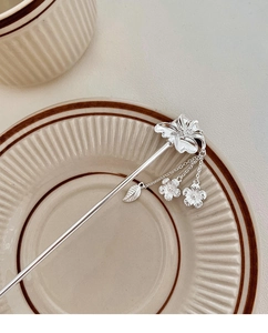 Détail d'un pic à cheveux floral argenté avec pampilles et breloques de feuilles sur plat